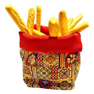 Op de afbeelding: Een broodmand gevuld met gouden breadsticks. De mand heeft een rode rand en een patroonstof met een mix van kleuren, waaronder blauw, geel en rood. De breadsticks zijn lang en dun.
