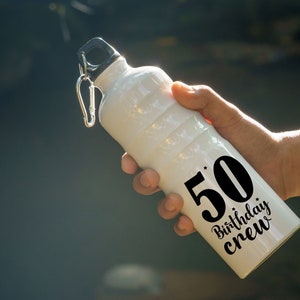 May include: White water bottle with a black lid and a black design that says "50 Birthday Crew".