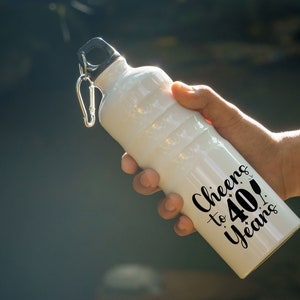 May include: White water bottle with a black lid and a black carabiner clip. The bottle has black text that reads "Cheers to 40 Years!"