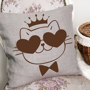 May include: A brown linen pillow with a cute cartoon cat wearing a crown and heart-shaped sunglasses. The cat is wearing a bow tie.