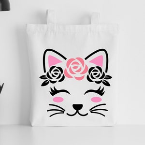 May include: White tote bag with a black and pink silhouette of a cat wearing a flower crown. The cat has closed eyes and a smiling mouth.