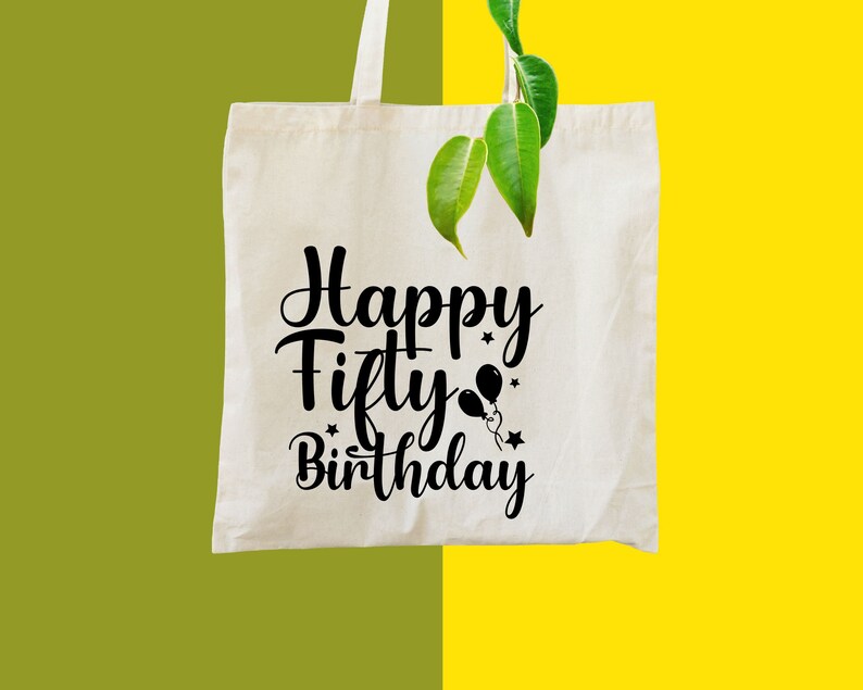 May include: A cream-colored tote bag with the words "Happy Fifty Birthday" in black script. The design includes balloon and star graphics. The bag is hanging with a green and yellow background.