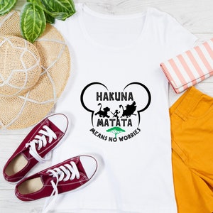 May include: White t-shirt with a black silhouette of characters from the movie The Lion King. The text "Hakuna Matata Means No Worries" is printed on the shirt.