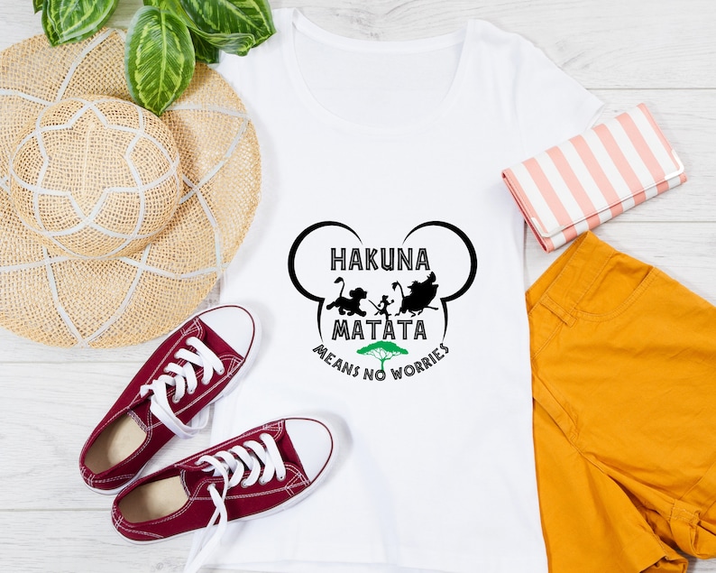 May include: White t-shirt with a black silhouette of characters from the movie The Lion King. The text "Hakuna Matata Means No Worries" is printed on the shirt.