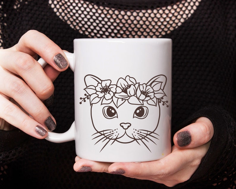 May include: White ceramic mug with a black and white illustration of a cat wearing a flower crown. The cat has large eyes and a cute expression.