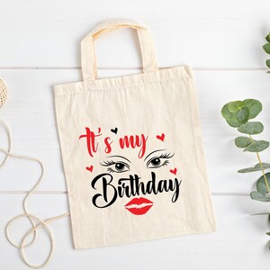K&ouml;nnte beinhalten: Eine wei&szlig;e Canvas-Tragetasche mit schwarzem Text, der "It's my Birthday" lautet, mit einem roten Lippenstift und Wimpern-Grafik.