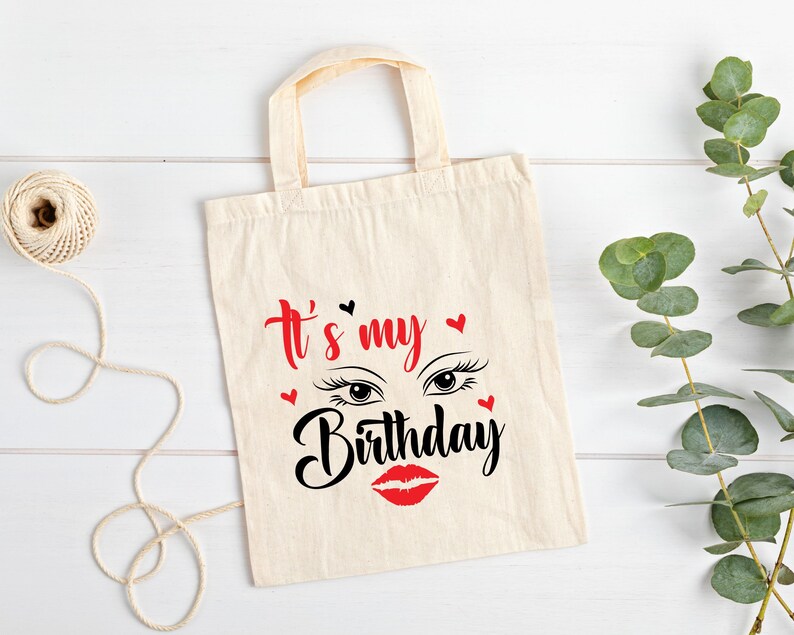 K&ouml;nnte beinhalten: Eine wei&szlig;e Canvas-Tragetasche mit schwarzem Text, der "It's my Birthday" lautet, mit einem roten Lippenstift und Wimpern-Grafik.