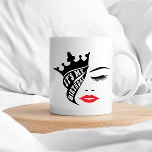 K&ouml;nnte beinhalten: Wei&szlig;e Keramiktasse mit einem schwarz-wei&szlig;en Design einer Krone, einem Frauenauge und dem Text "It's My Birthday". Die Lippen der Frau sind rot.
