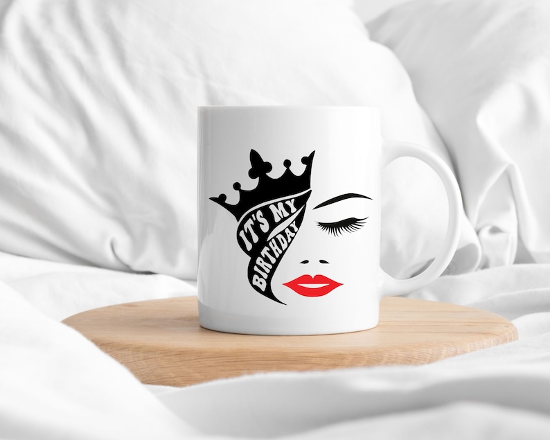 K&ouml;nnte beinhalten: Wei&szlig;e Keramiktasse mit einem schwarz-wei&szlig;en Design einer Krone, einem Frauenauge und dem Text "It's My Birthday". Die Lippen der Frau sind rot.