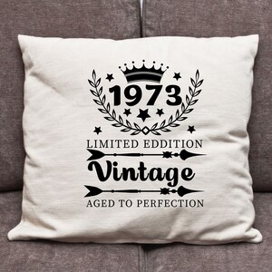 May include: White throw pillow with black text and a crown graphic. The text reads "1973 Limited Edition Vintage Aged to Perfection".