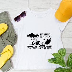 May include: White t-shirt with a black graphic of the Lion King characters Simba, Timon, and Pumbaa. The text "Hakuna Matata" and "It means no worries" is printed below the graphic.