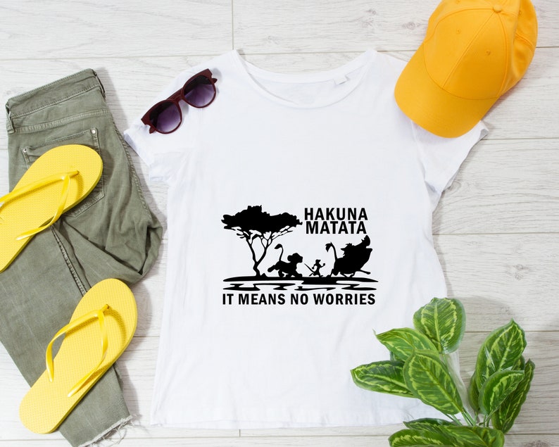 May include: White t-shirt with a black graphic of the Lion King characters Simba, Timon, and Pumbaa. The text "Hakuna Matata" and "It means no worries" is printed below the graphic.