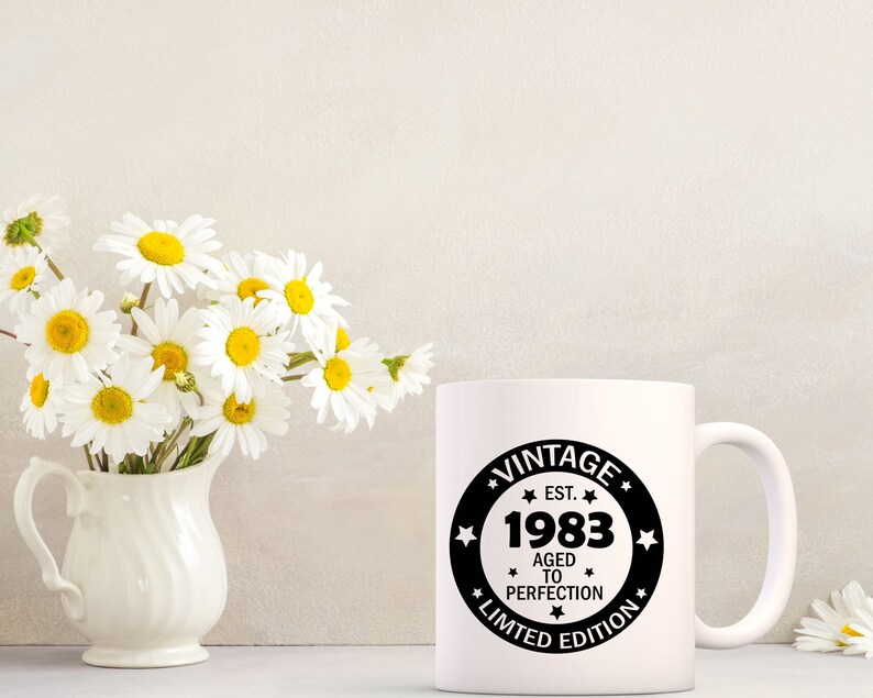May include: White ceramic mug with a black circle design that says "Vintage Est. 1983 Aged to Perfection Limited Edition".