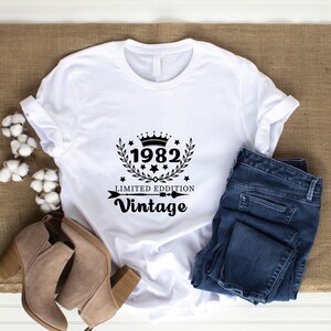May include: White t-shirt with black text and a crown graphic. The text reads "1982 Limited Edition Vintage".