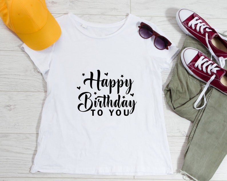 K&ouml;nnte beinhalten: Wei&szlig;es T-Shirt mit schwarzem Text, der "Happy Birthday to You" mit kleinen Herzen und Sternen um den Text herum sagt.