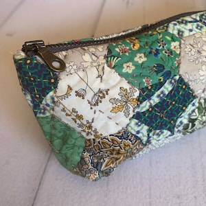 May include: A green and white patchwork fabric pencil case with a zipper closure. The case is made of different floral and geometric patterns.