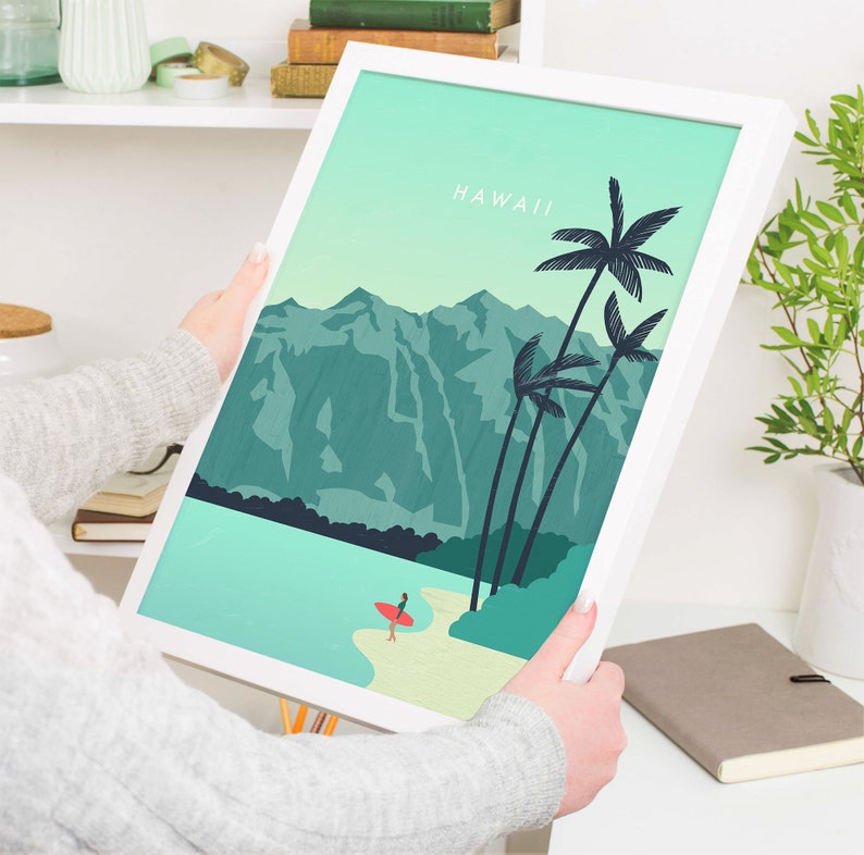 May include: A white framed print with a teal and green landscape scene of mountains, palm trees, and a beach with a person surfing. The text "HAWAII" is at the top of the print.
