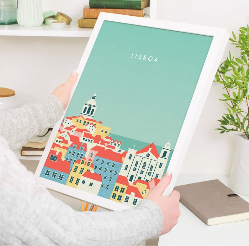 May include: A framed art print featuring a stylized illustration of Lisbon, Portugal. The artwork depicts colorful buildings with red, yellow, and blue roofs against a teal background. The word "LISBOA" is printed at the top.