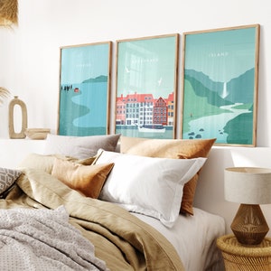 May include: Three framed art prints with Scandinavian-style illustrations. The prints feature landscapes with the words "SVERIGE", "KOBENHAVN", and "ISLAND". The prints are displayed above a bed with neutral-toned bedding and decorative pillows.