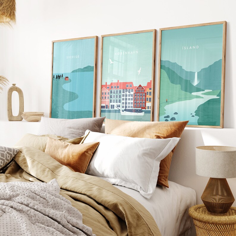 May include: Three framed art prints with Scandinavian-style illustrations. The prints feature landscapes with the words "SVERIGE", "KOBENHAVN", and "ISLAND". The prints are displayed above a bed with neutral-toned bedding and decorative pillows.