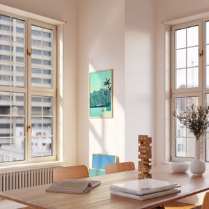 May include: A wooden table with a stack of books, a game of blocks, and a framed print of a tropical landscape with palm trees and mountains. The table is set with a white bowl and a white vase with green branches.