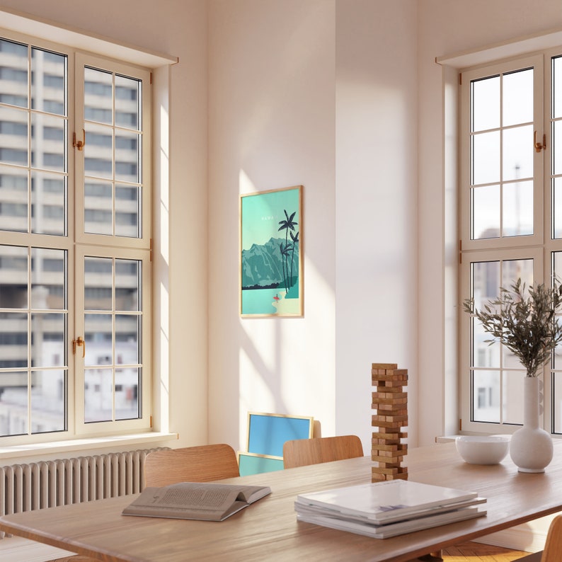 May include: A wooden table with a stack of books, a game of blocks, and a framed print of a tropical landscape with palm trees and mountains. The table is set with a white bowl and a white vase with green branches.