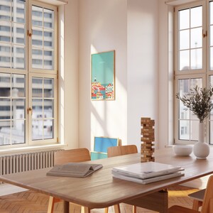 May include: A room with a wooden dining table, chairs, and a framed print on the wall. The print features a colorful illustration of a cityscape with the word "LISBON" at the top. A stack of wooden blocks and a vase with greenery are on the table.