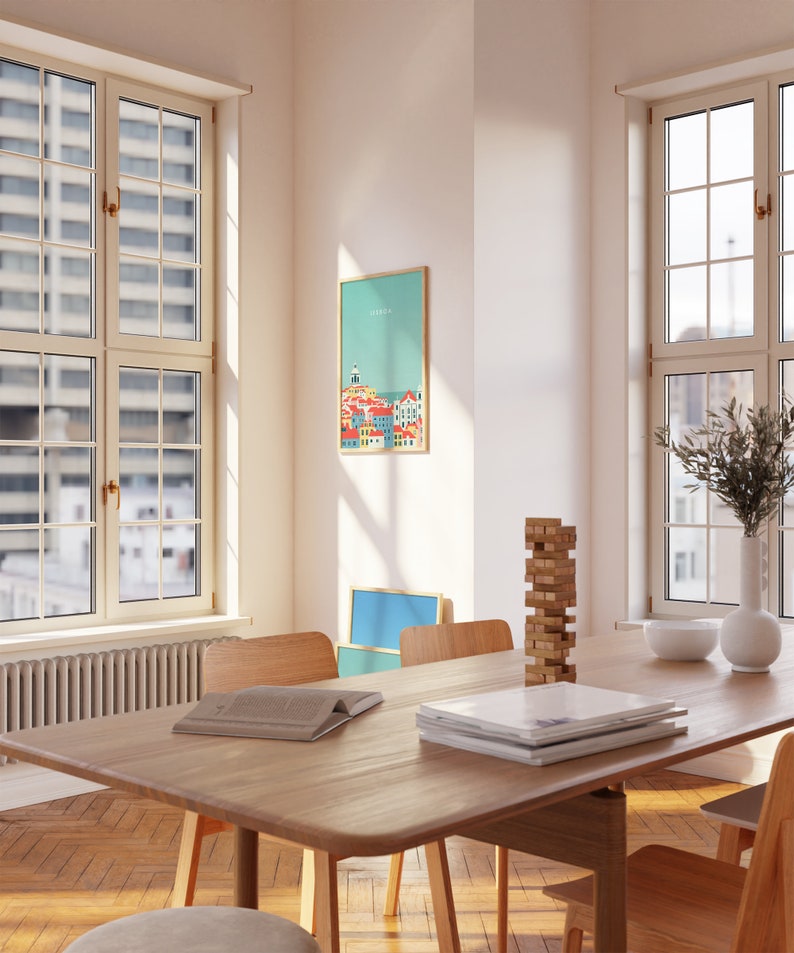 May include: A room with a wooden dining table, chairs, and a framed print on the wall. The print features a colorful illustration of a cityscape with the word "LISBON" at the top. A stack of wooden blocks and a vase with greenery are on the table.
