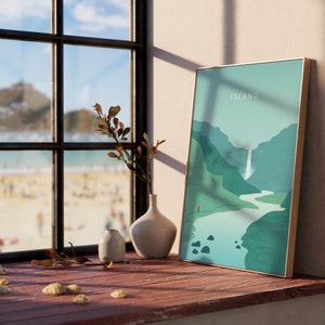 May include: A framed art print with the word "ISLAND" in white text. The artwork depicts a landscape with mountains, a waterfall, and a river in shades of green and blue. A small figure stands at the bottom. The frame is gold.