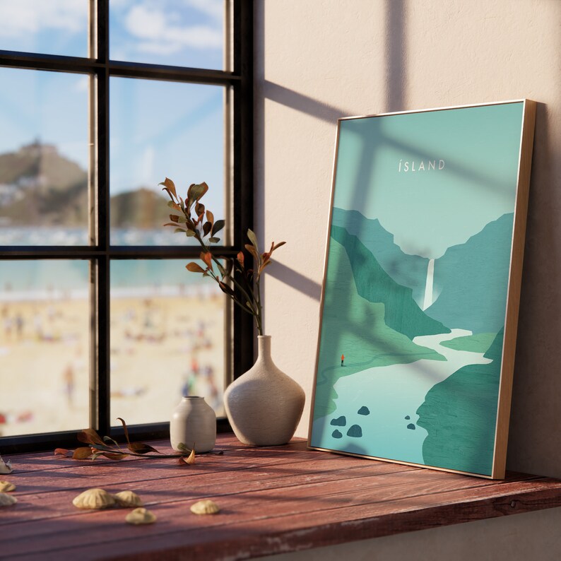 May include: A framed art print with the word "ISLAND" in white text. The artwork depicts a landscape with mountains, a waterfall, and a river in shades of green and blue. A small figure stands at the bottom. The frame is gold.