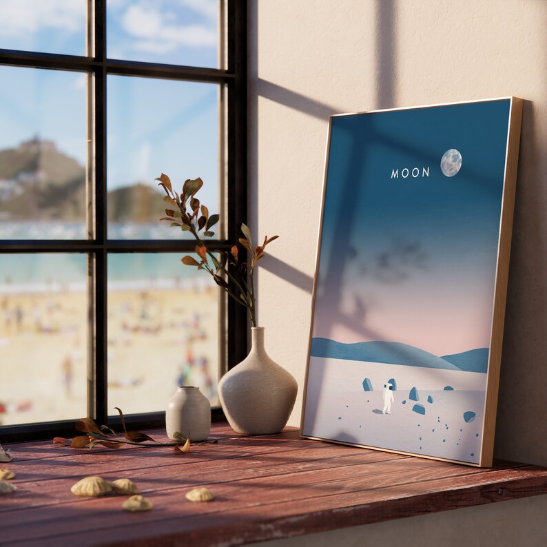 K&ouml;nnte beinhalten: Ein gerahmter Druck mit einer blauen, rosa und wei&szlig;en Landschaftsszene. Der Druck zeigt einen einsamen Astronauten, der auf einer mond&auml;hnlichen Oberfl&auml;che steht. Der Text "MOON" ist oben auf dem Druck in Wei&szlig; gedruckt.