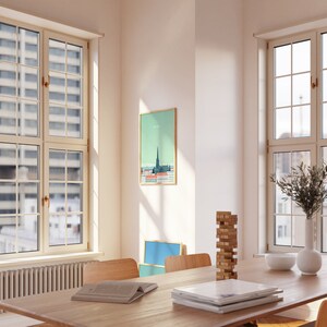May include: A wooden table with a stack of books, a wooden block tower game, and a white bowl on a light wood surface. There is a framed print of a city skyline on the wall behind the table. The room has large windows with white trim.