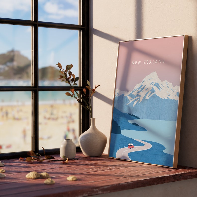 May include: A framed print of a mountain landscape with a red car driving on a winding road. The print has a pink sky and blue mountains with the text "NEW ZEALAND" at the top.