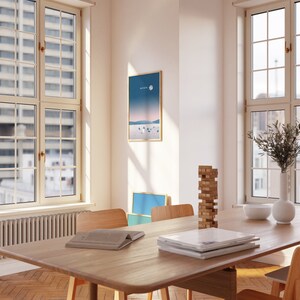 K&ouml;nnte beinhalten: Ein Esstisch aus Holz mit einer hellen Holzoptik. Auf dem Tisch liegen ein Stapel B&uuml;cher und ein Turm aus Holzkl&ouml;tzen. Es gibt vier St&uuml;hle um den Tisch herum, von denen zwei auf dem Bild zu sehen sind. Der Tisch steht in einem Raum mit gro&szlig;en Fenstern und einem gerahmten Druck an der Wand.