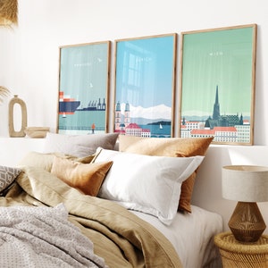 May include: Three framed city skyline prints with a minimalist design. The prints feature the cities of Hamburg, Zurich, and Wien. The prints are hung on a white wall above a bed with brown bedding.
