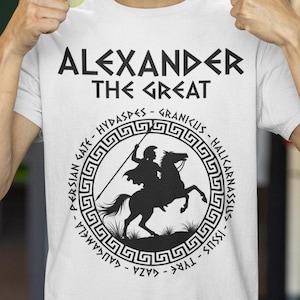 May include: White t-shirt with a black graphic of Alexander the Great on horseback. The graphic includes a Greek key border and the text "Alexander the Great" and a list of battles: "Persian Gate - Hydaspes - Granicus - Halicarnassus - Issus - Tyre - Gaza - Gaugamela"