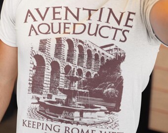 Op de afbeelding: Een wit T-shirt met een bruine afbeelding van de Aqueducts van de Aventine in Rome, Italië. De tekst "Keeping Rome Wet Since 312 BC" is onder de afbeelding gedrukt.