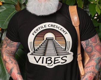 Op de afbeelding: Een zwart T-shirt met een afbeelding van een piramide met een zonsondergang erachter. De tekst "Fertile Crescent Vibes" staat op het shirt gedrukt.