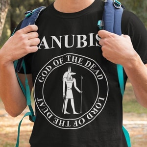 Op de afbeelding: Een zwart T-shirt met een witte afbeelding van Anubis, de Egyptische god van de dood. De afbeelding is een cirkel met de woorden "God van de Doden" en "Heer van de Duat" rondom de afbeelding van Anubis.