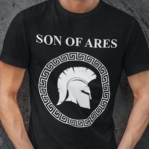 May include: A black t-shirt with a white graphic of a Spartan helmet inside a circle of Greek key design. The text "SON OF ARES" is printed above the graphic.