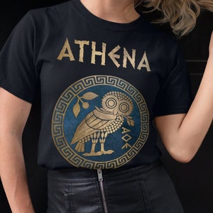May include: A black t-shirt featuring a gold graphic of the Greek goddess Athena's owl and the word "ATHENA" in gold lettering.