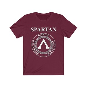 May include: A maroon t-shirt with a white graphic of a Spartan shield with the words "SPARTAN", "HONOR", "STRENGTH", "DISCIPLINE" around the shield.