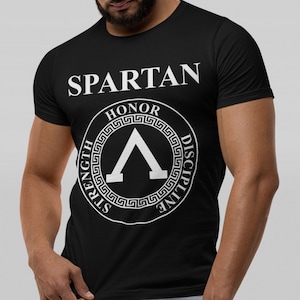 Könnte beinhalten: Schwarzes T-Shirt mit einem weißen Grafikdruck eines spartanischen Helms mit den Worten "Spartan", "Ehre", "Stärke" und "Disziplin" drumherum.
