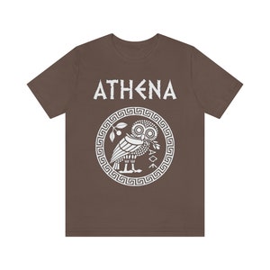 May include: A brown t-shirt with a white graphic of the Greek goddess Athena. The graphic features an owl with an olive branch in its beak, surrounded by a Greek key border. The text "ATHENA" is above the graphic.