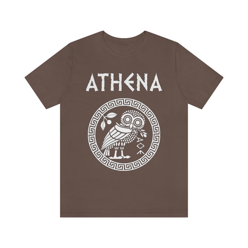 May include: A brown t-shirt with a white graphic of the Greek goddess Athena. The graphic features an owl with an olive branch in its beak, surrounded by a Greek key border. The text "ATHENA" is above the graphic.