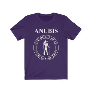Op de afbeelding: Paars T-shirt met korte mouwen met een witte afbeelding van Anubis, de Egyptische god van de dood. De afbeelding bevat de tekst "Anubis, God van de Doden, Heer van de Duat".