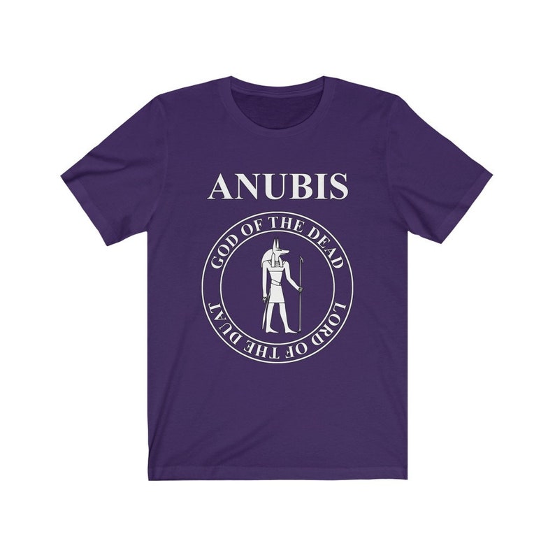 Op de afbeelding: Paars T-shirt met korte mouwen met een witte afbeelding van Anubis, de Egyptische god van de dood. De afbeelding bevat de tekst "Anubis, God van de Doden, Heer van de Duat".