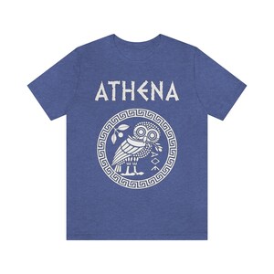 May include: A blue t-shirt with a white graphic of the Greek goddess Athena. The graphic features an owl with an olive branch in its beak, surrounded by a circular design with a Greek key pattern. The text "ATHENA" is printed above the graphic.