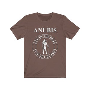 Op de afbeelding: Een bruin t-shirt met een witte afbeelding van Anubis, de Egyptische god van de dood. De afbeelding bevat de tekst "Anubis, God van de Doden, Heer van de Duat".