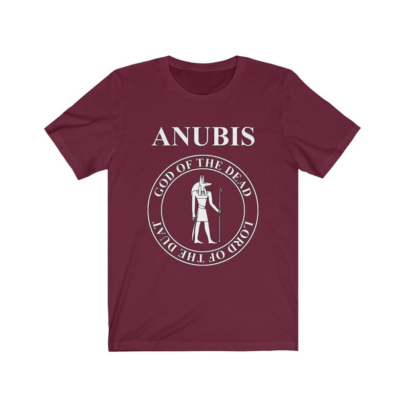 Op de afbeelding: Een maroon t-shirt met een witte afbeelding van Anubis, de Egyptische god van de dood. De afbeelding bevat de tekst "Anubis, God van de Doden, Heer van de Duat".